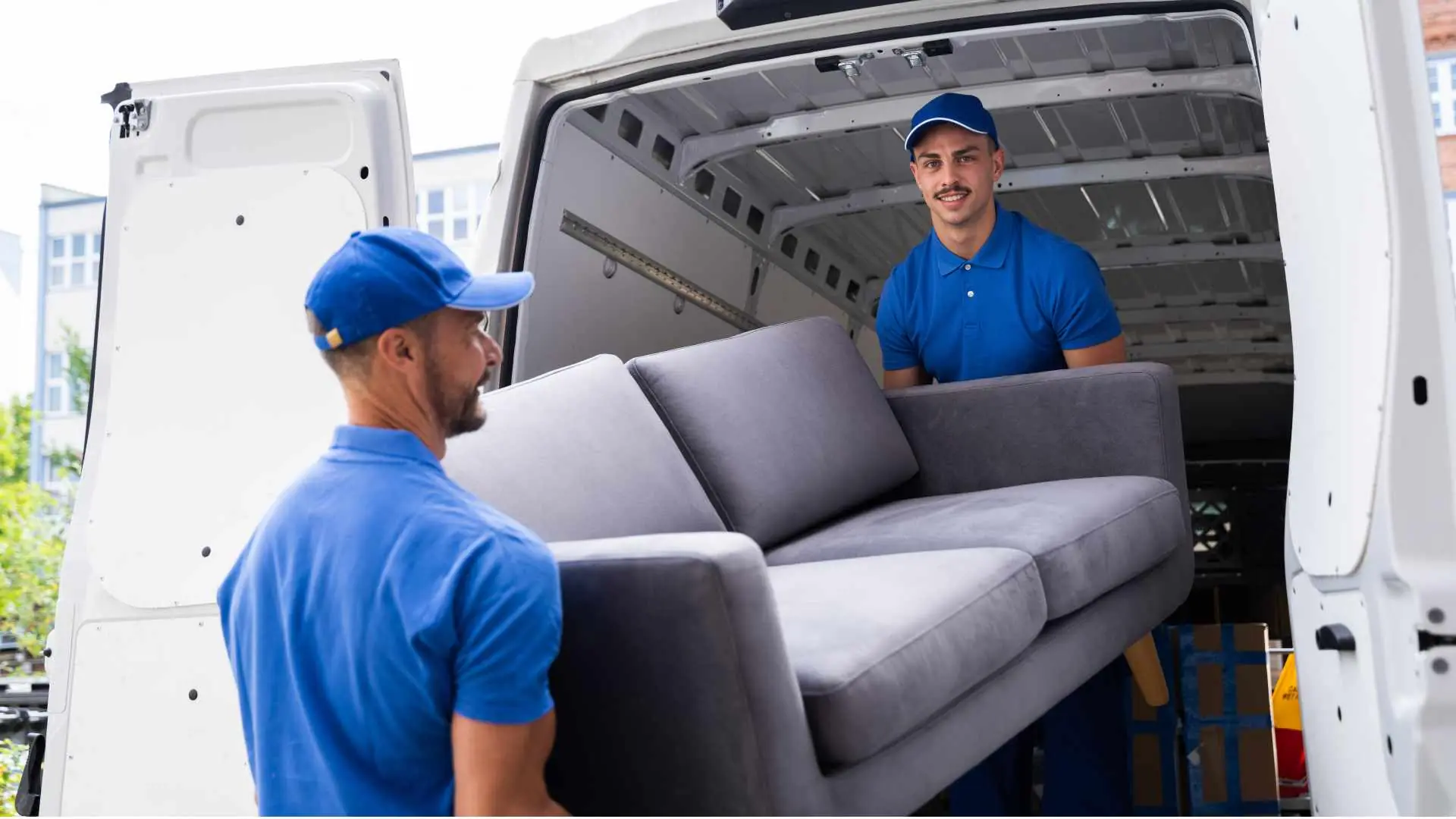 Two individuals removing a gray sofa from the back of a white van - demolition services, house demolition, affordable junk removal, junk removal quote, junk removal New York