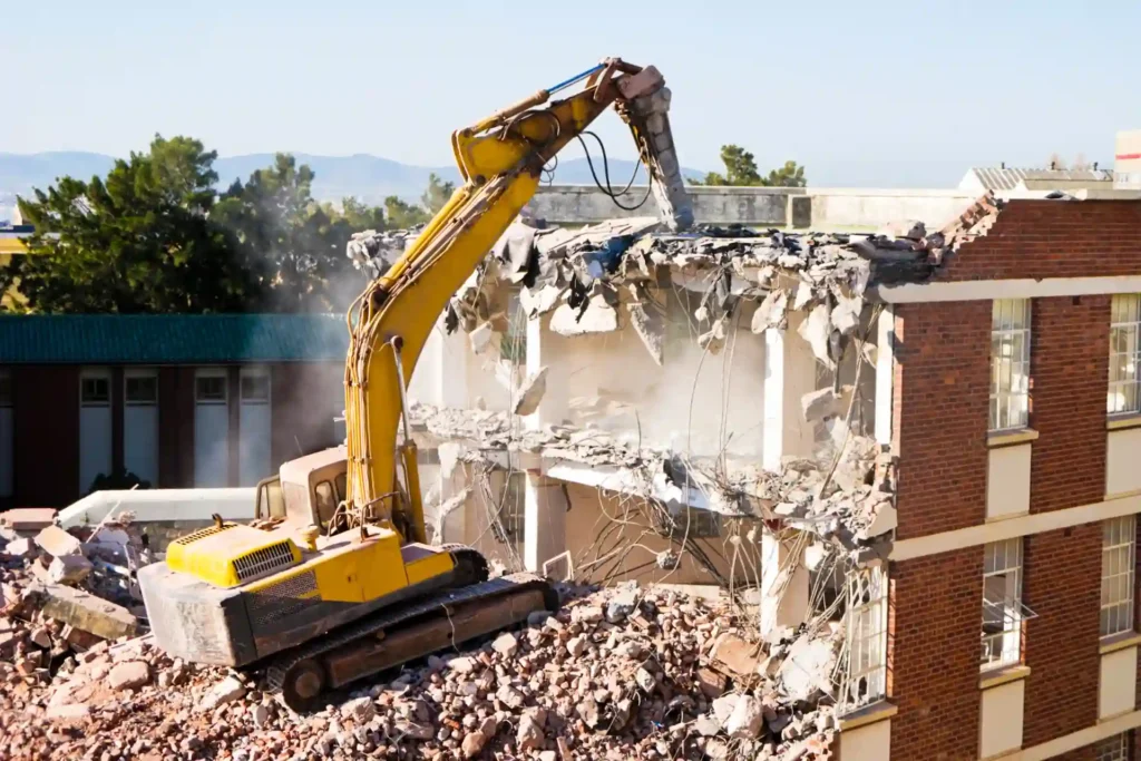 Commercial Demolition - Large yellow excavator with an extended arm tearing down a multi-story building