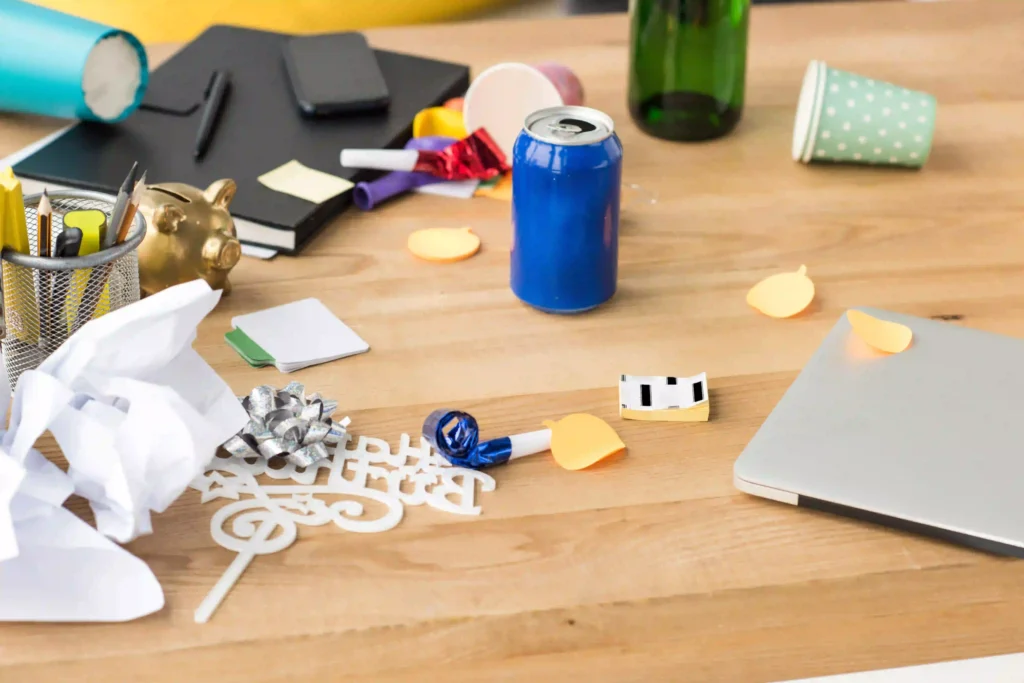 Office Junk Removal - Cluttered office desk with various items including crumpled paper, bottles, and an open laptop